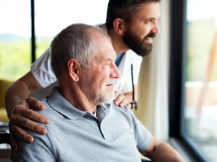 A male healthcare worker talking to senior man in wheelchair indoors at home
