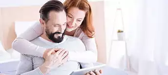 woman hugging man while he looks at tablet