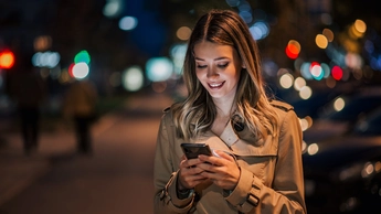 Portrait of a smiling young woman using smart phone at night