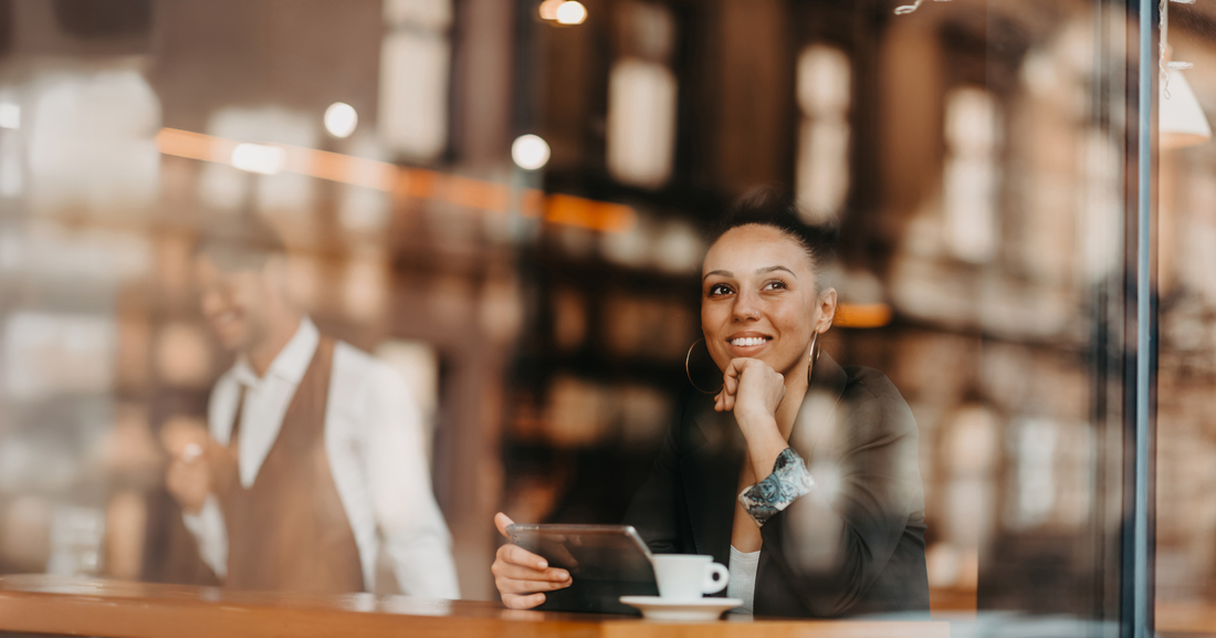 woman in a coffee shop drink coffee viewed through glass with reflections as they sit at a table chatting and laughing