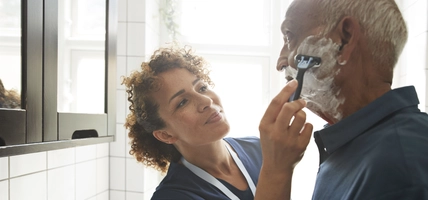 Healthcare worker assisting senior man in shaving