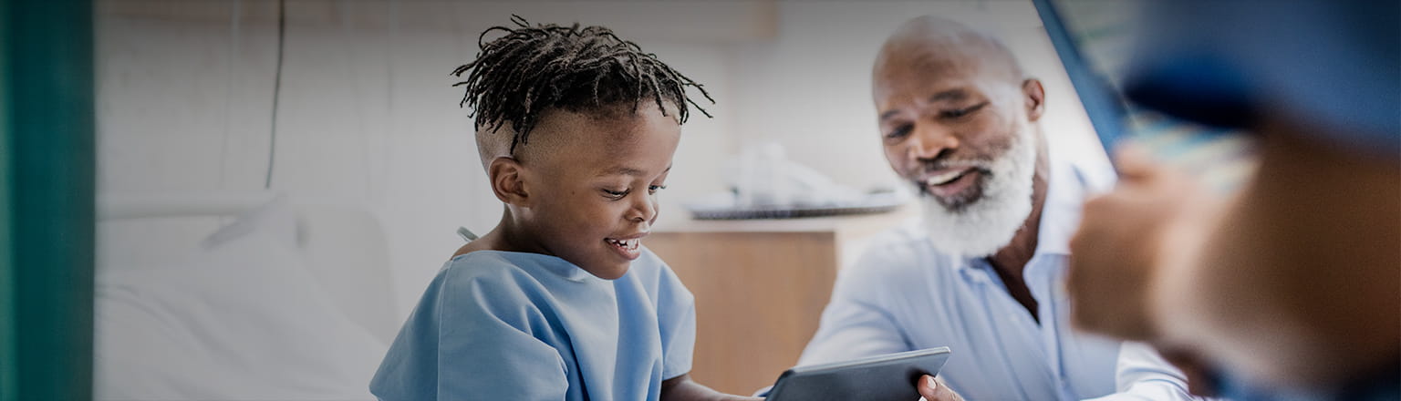 kid patient on hospital bed smiling when her family member shows her a notepad screen