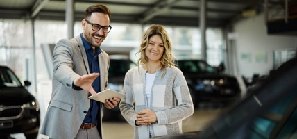 Happy salesman selling the car to his female customer in a showroom