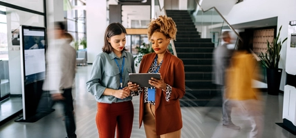 Female coworkers discussing work with people in blurred motion behind