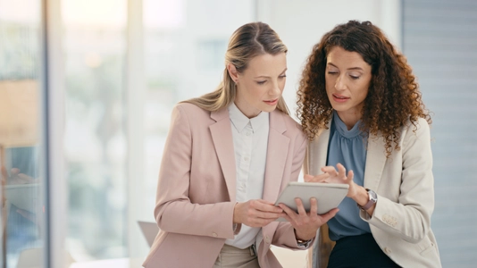 Tablet, teamwork and meeting with a business woman and colleague talking about an idea in their office together