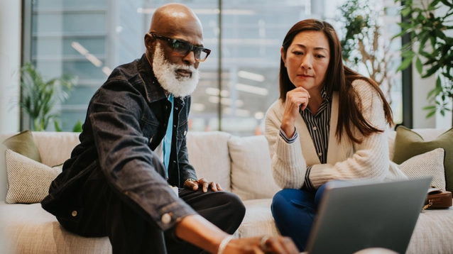 A man and a woman on a stylish white sofa in a contemporary office building have a casual business meeting