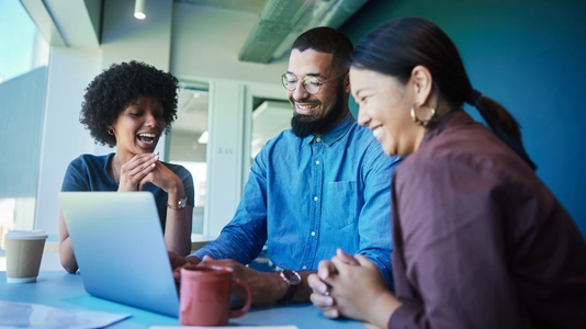 Diverse young businesspeople talking and laughing while working on a laptop 