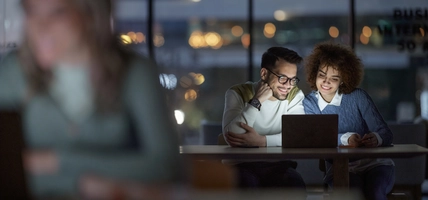 Happy entrepreneurs reading an e-mail on laptop late in the office.
