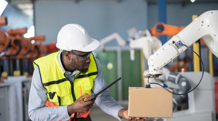 Engineer working with robotic arm picking up package at industrial manufacturing