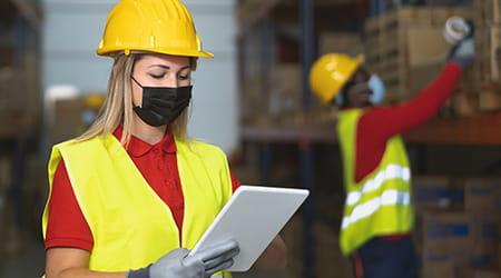 Two workers in a manufacturing facility with hard hats and computer