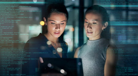 Two women compare computer screens