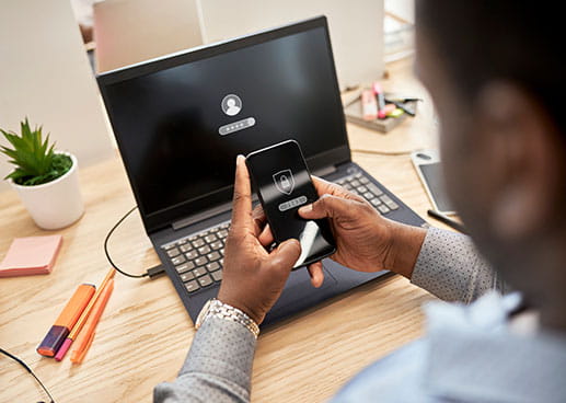 man unlocking his phone with laptop in background