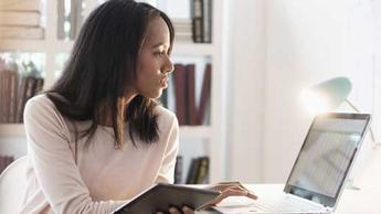 woman working at computer while holding tablet