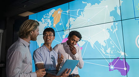 three colleagues looking at regions on a map on a digital screen