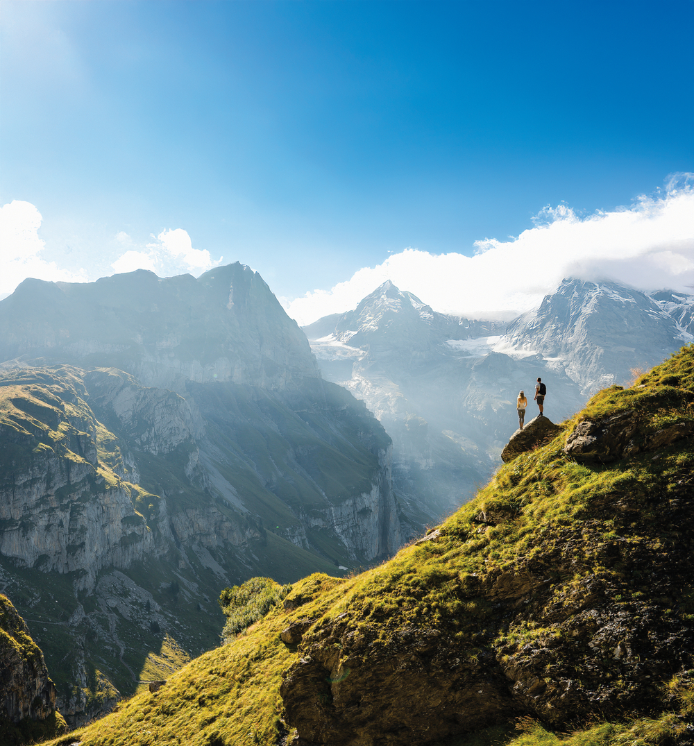 An adventurous man stands on top of a mountain and enjoys a beautiful view during sunny summer day,  Beautiful nature with steep mountains and rocks in background. Swiss Alps. Discover