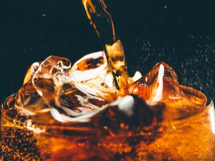 A glass of cold cola with ice cubes. Pouring cola close up.