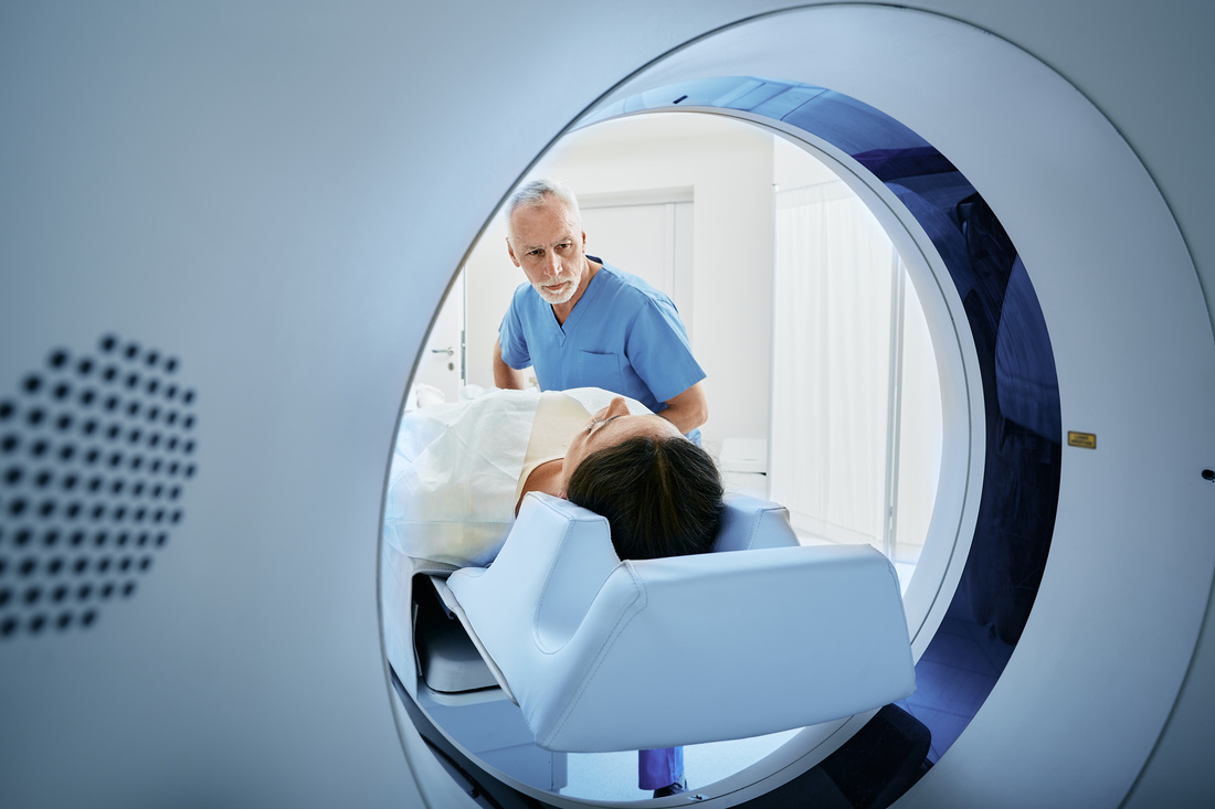 CT scan technologist overlooking patient in Computed Tomography scanner during preparation for procedure. Woman patient going into CT scanner
