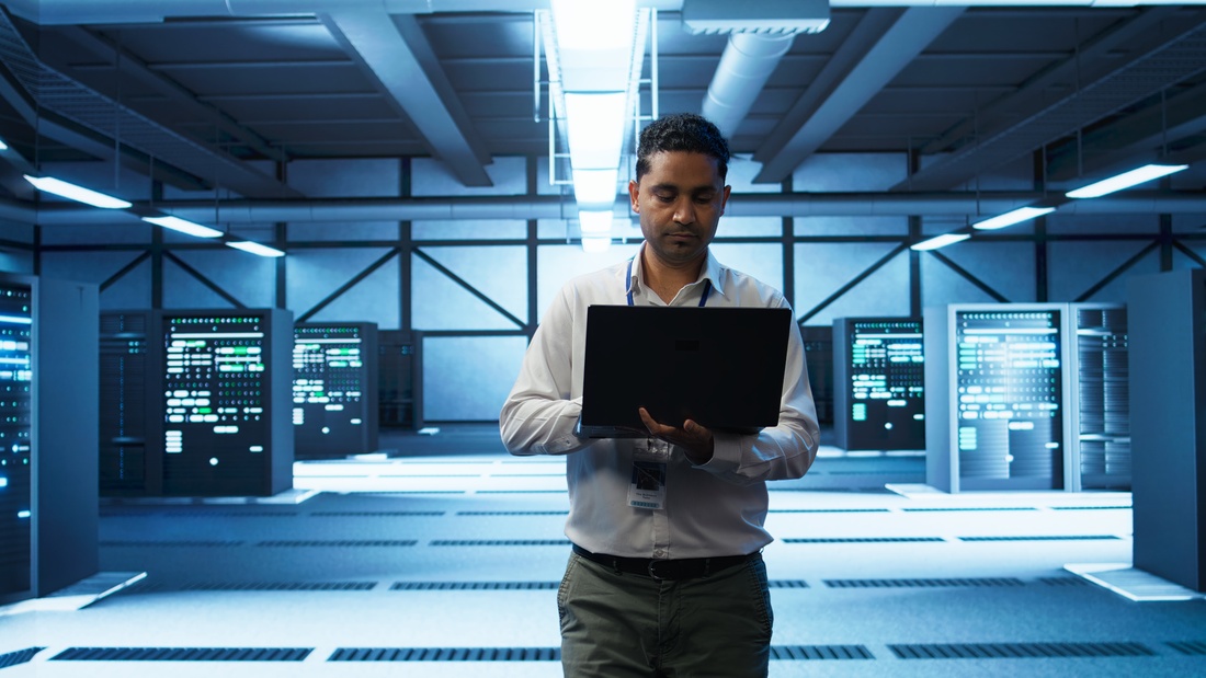 Technician using laptop in data center, managing servers
