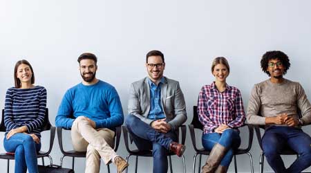 A groups of young professionals sitting in a row with their legs crossed. They are all smiling.