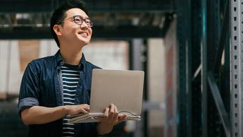 Man in warehouse holding laptop smiling