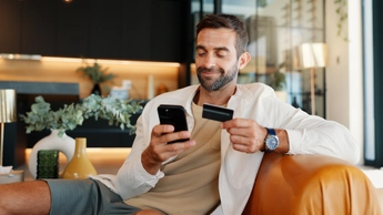 Credit card, mobile and happy man with payment in home for online shopping, internet banking or purchase. Phone, debit and person with digital money in living room for ecommerce, finance or deposit