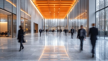 Blurred motion of diverse business people walking through a modern building's bright, spacious lobby. 