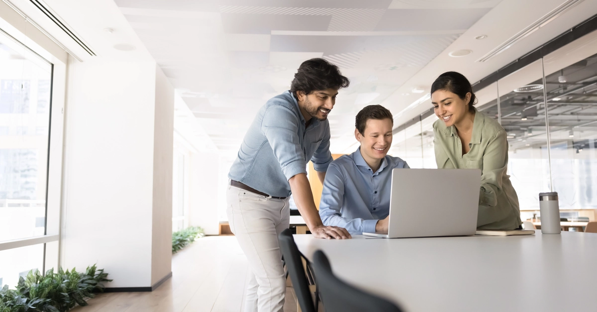 Three colleagues gathered around laptop in modern coworking space