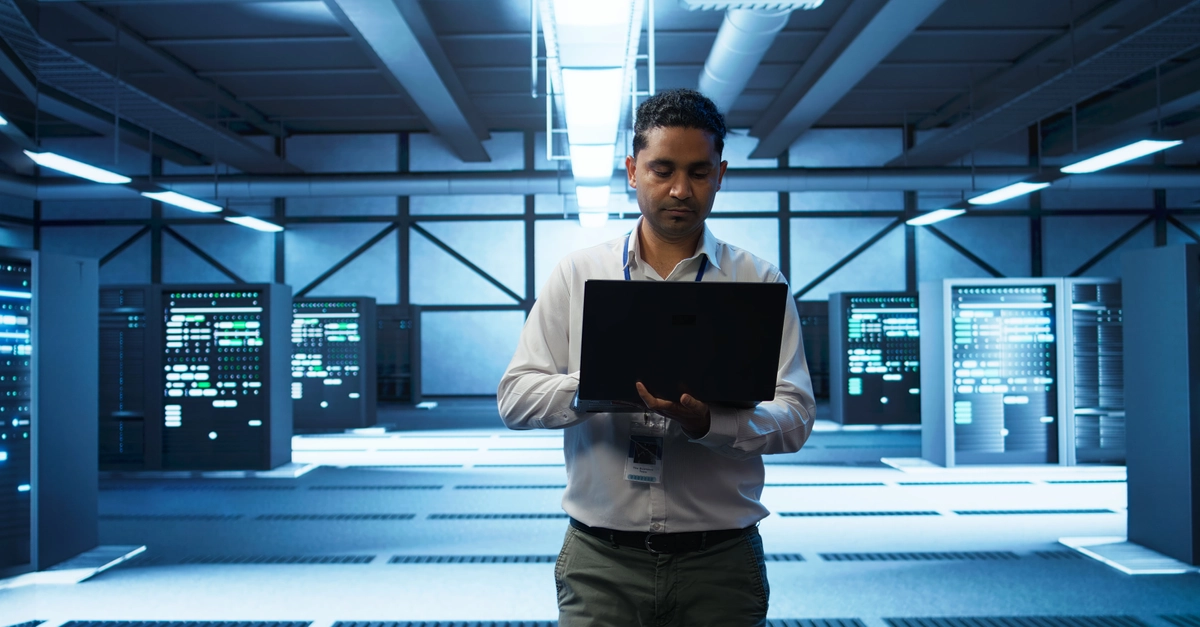 Technician using laptop in data center, managing servers