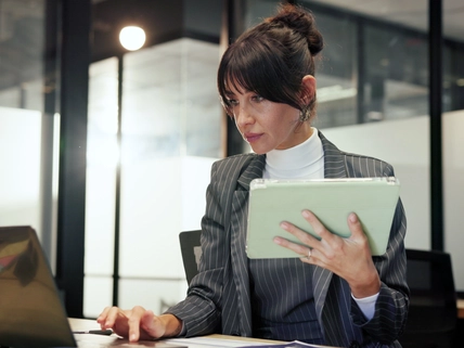 woman holding tablet while working on laptop