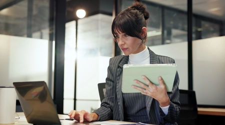 woman holding tablet while working on laptop