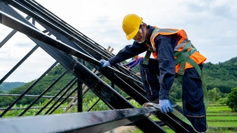 Construction worker wearing safety harness using secondary safety device connecting into 15 mm static rope using as fall restraint shingle on top of the new roof.