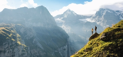 An adventurous man stands on top of a mountain and enjoys a beautiful view during sunny summer day,  Beautiful nature with steep mountains and rocks in background. Swiss Alps. Discover