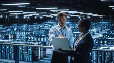 two people standing in server room looking at laptop