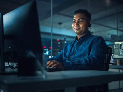 man workingNight Office: Portrait of Handsome Indian Man in Working on Desktop Computer. Digital Entrepreneur Typing, Creating Modern Software, e-Commerce App Design, Programming. Successful Smiling Man at computer screen