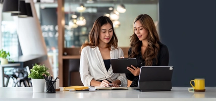Two young Asian business woman talk, consult, discuss working with new startup project idea presentation analyze plan marketing and investment in the office.