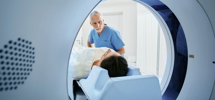 CT scan technologist overlooking patient in Computed Tomography scanner during preparation for procedure. Woman patient going into CT scanner