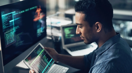 man working on tablet with computer screen in background