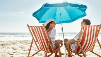 couple sitting on beach under blue umbrella