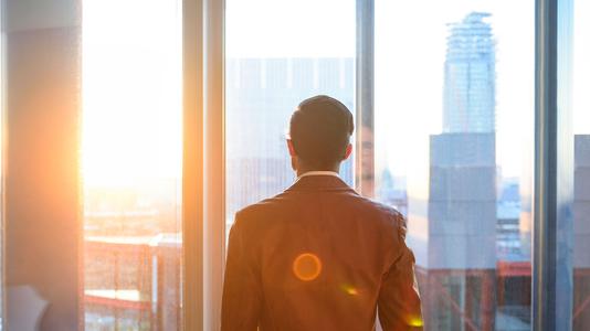 Businessman looking through office window in sunlight