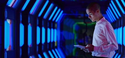 man in colorfully lit hallway looks at device