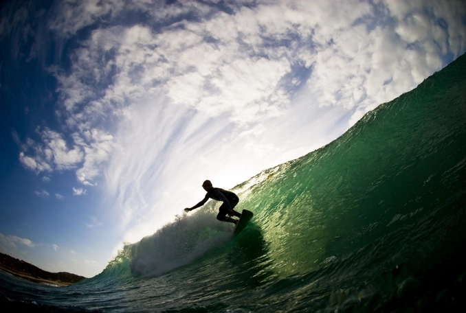 Ocean and cloudy sky with silhouette of surfer