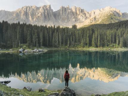 woman standing and looking at lake in valley surrounded by trees and mountains