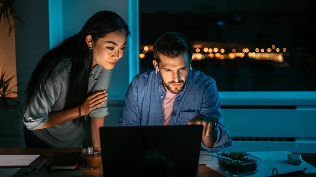 two people looking at a laptop screen in the evening