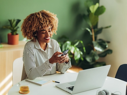 Happy African American woman typing text message on her smartphone while sitting at office desk