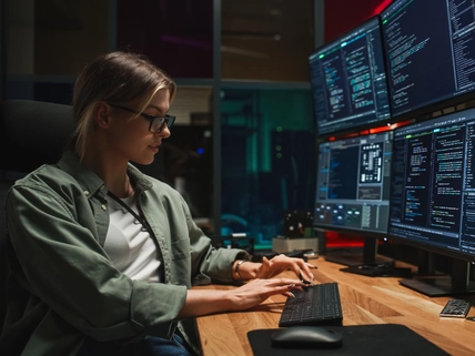 Programmer coding on monitors setup in dark office.