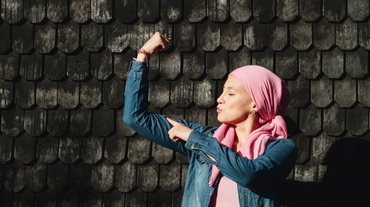 Woman with cancer showing strength with arms outdoors