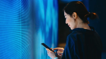 Woman using smartphone against blue coloured LED digital display screen