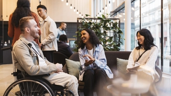 Happy businesswomen discussing with male entrepreneur sitting on wheelchair at convention center