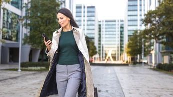 A businesswoman in a trench coat walks through a modern city plaza during the morning