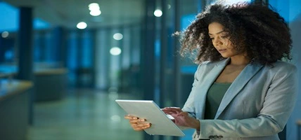 A young female businesswoman sits in a modern business interior looking at her digital tablet